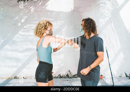 Man and woman wearing mask giving elbow bump while standing against wall Stock Photo