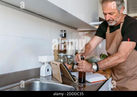 Mature man opening beer bottle while standing in kitchen Stock Photo