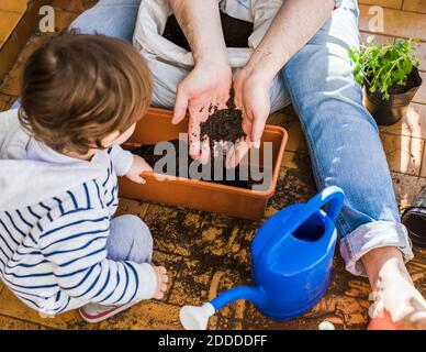 Mother and son putting mud in pot while sitting at balcony Stock Photo