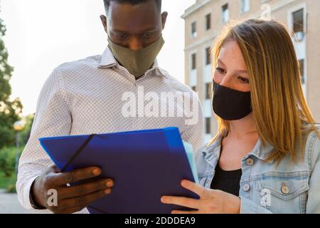 Male and female university students wearing protective face mask while discussing in campus Stock Photo