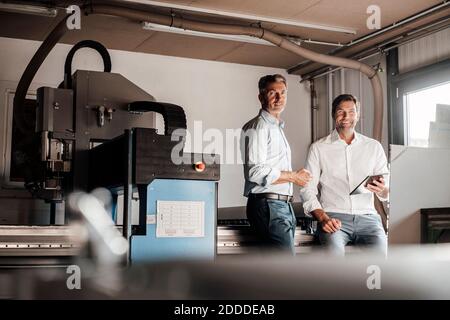 Smiling male engineer with digital tablet by colleague in industry Stock Photo