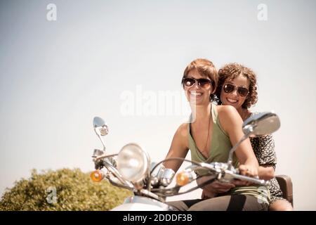 Female friends riding on motorcycle during sunny day Stock Photo