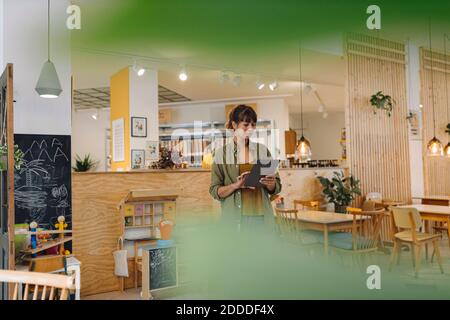 Female owner using digital tablet while standing in coffee shop Stock Photo