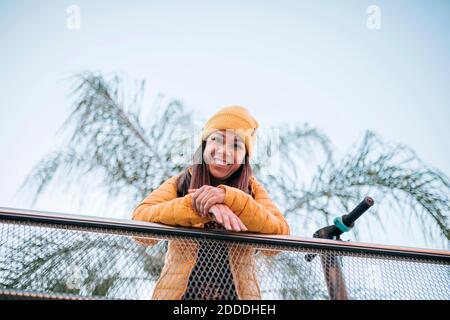 Cheerful mature woman leaning on railing against sky Stock Photo