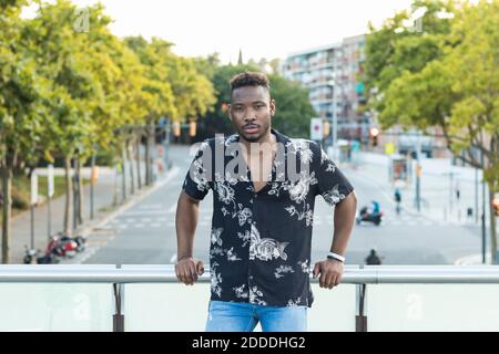 Young man leaning on railing at bridge over street in city Stock Photo