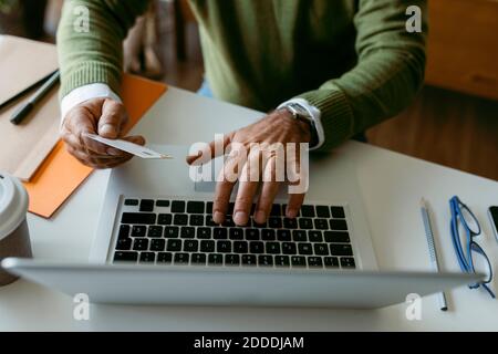 Midsection of man using credit card while working on laptop at home Stock Photo