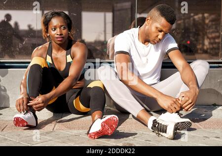 Athletes tying shoelaces while sitting on sidewalk at city Stock Photo