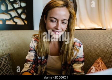 Smiling businesswoman looking at laptop while sitting on sofa at home Stock Photo