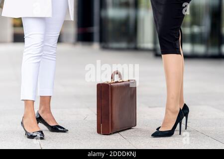 Businesswomen standing by briefcase on footpath Stock Photo