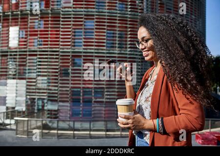 Smiling woman sending voicemail through smart phone while standing in city during sunny day Stock Photo