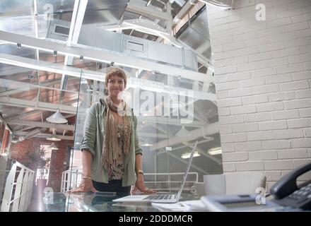 Smiling young woman standing by table at office Stock Photo