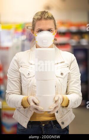 Teenage girl wearing protectice mask and gloves holding stack of four toilet rolls at supermarket Stock Photo