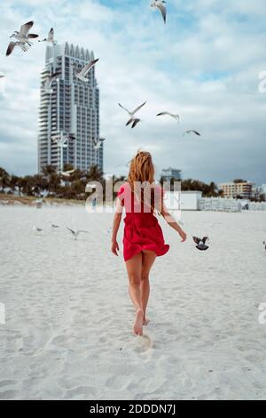 Seagull flying while woman walking on sand against sky at beach Stock Photo