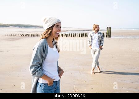 Cheerful young woman standing with hands in pockets at beach during sunny day Stock Photo