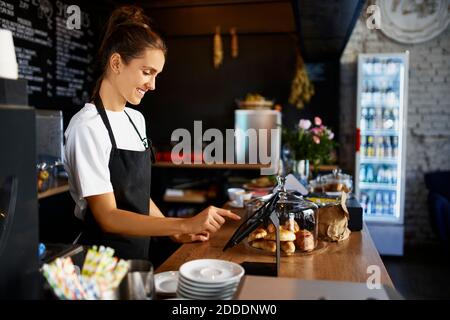 Smiling barista using digital tablet at kitchen counter in cafe Stock Photo