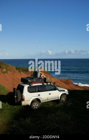 Mid adult couple sitting on 4x4 roof while looking at sea against blue sky