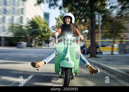 Cheerful woman riding motor scooter on street in city Stock Photo