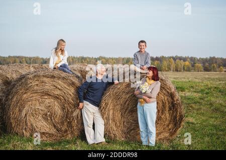 Senior couple with grandchildren sitting on hay bales on field during weekend Stock Photo