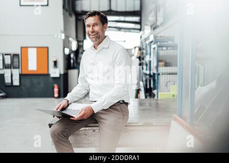 Smiling male engineer using laptop while sitting on table in industry Stock Photo