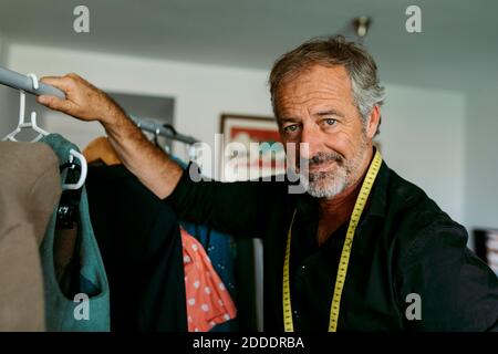 Smiling mature male tailor by rack at workplace Stock Photo