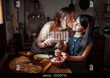 Mother kissing daughter while standing in kitchen at home Stock Photo