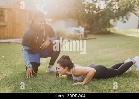 Smiling man motivating woman doing push ups at backyard Stock Photo