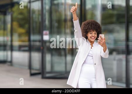 Businesswoman showing thumps up while using mobile phone outdoors Stock Photo