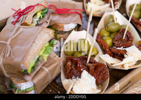 Sandwiches with meat and vegetables and baskets with dried tomatoes, green olives and cheese on a wooden tray Stock Photo