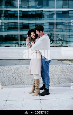 Smiling man embracing female partner while standing against building in city Stock Photo
