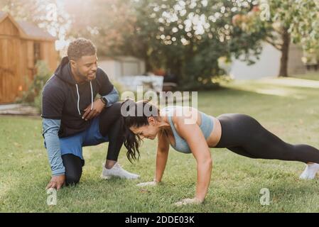 Smiling man looking at woman doing push ups at backyard Stock Photo