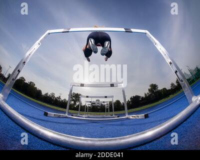 Athlete jumping over hurdle on track at training ground Stock Photo