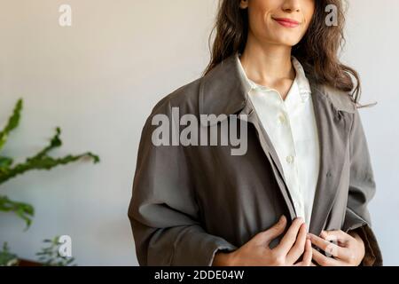 Smiling female model wearing jacket standing against wall Stock Photo