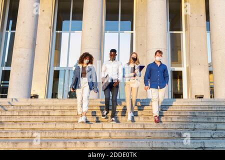University students wearing protective face mask while moving down on staircase against education building Stock Photo