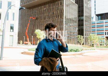 Handsome young businessman talking on smart phone while walking on footpath in city Stock Photo
