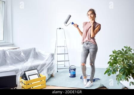 Thoughtful woman with head in hands holding paint roller while standing at home Stock Photo