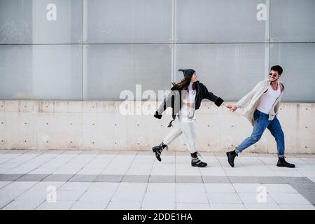 Smiling man holding hands with female partner while walking on sidewalk Stock Photo