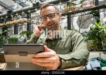 Businessman adjusting in-ear headphones while using digital tablet at cafe Stock Photo
