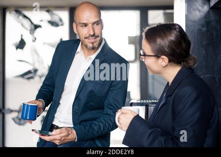 Businessman and woman with coffee cup using mobile phone while standing at office Stock Photo