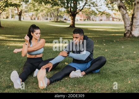 Couple doing warm up exercise while sitting on grass at backyard Stock Photo