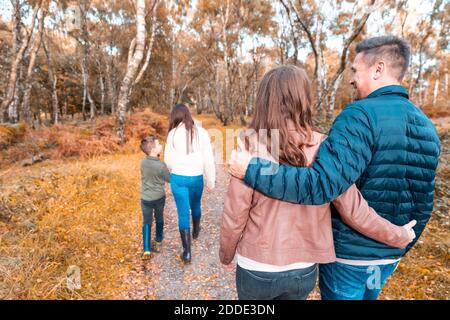 Parents with arms around walking behind children in park during autumn Stock Photo