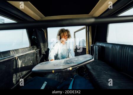 Smiling woman removing surfboard from car while standing at beach Stock Photo