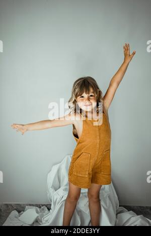 Cute girl with arms outstretched standing against wall at home Stock Photo