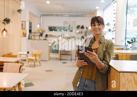 Smiling female owner using digital tablet standing in coffee shop Stock Photo