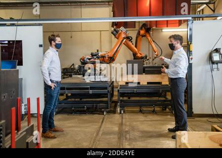 Businessmen wearing face mask standing with social distance against robotic machine at factory Stock Photo
