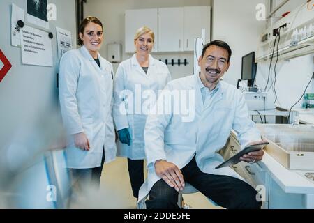 Scientist using digital tablet with coworkers standing behind at laboratory Stock Photo