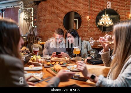 Women talking while drinking wine with friends using mobile phone in background at restaurant Stock Photo