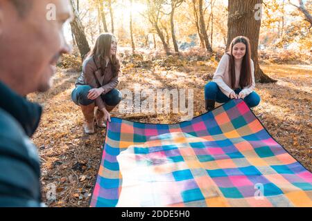 Family laying down picnic blanket in park during autumn Stock Photo