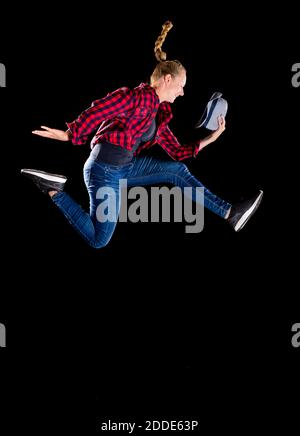 Young woman jumping while holding bowler hat against black background Stock Photo