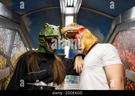 Male and female friends wearing dinosaur mask while traveling in train Stock Photo