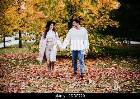 Smiling young couple holding hands while looking at each other against tree during autumn Stock Photo